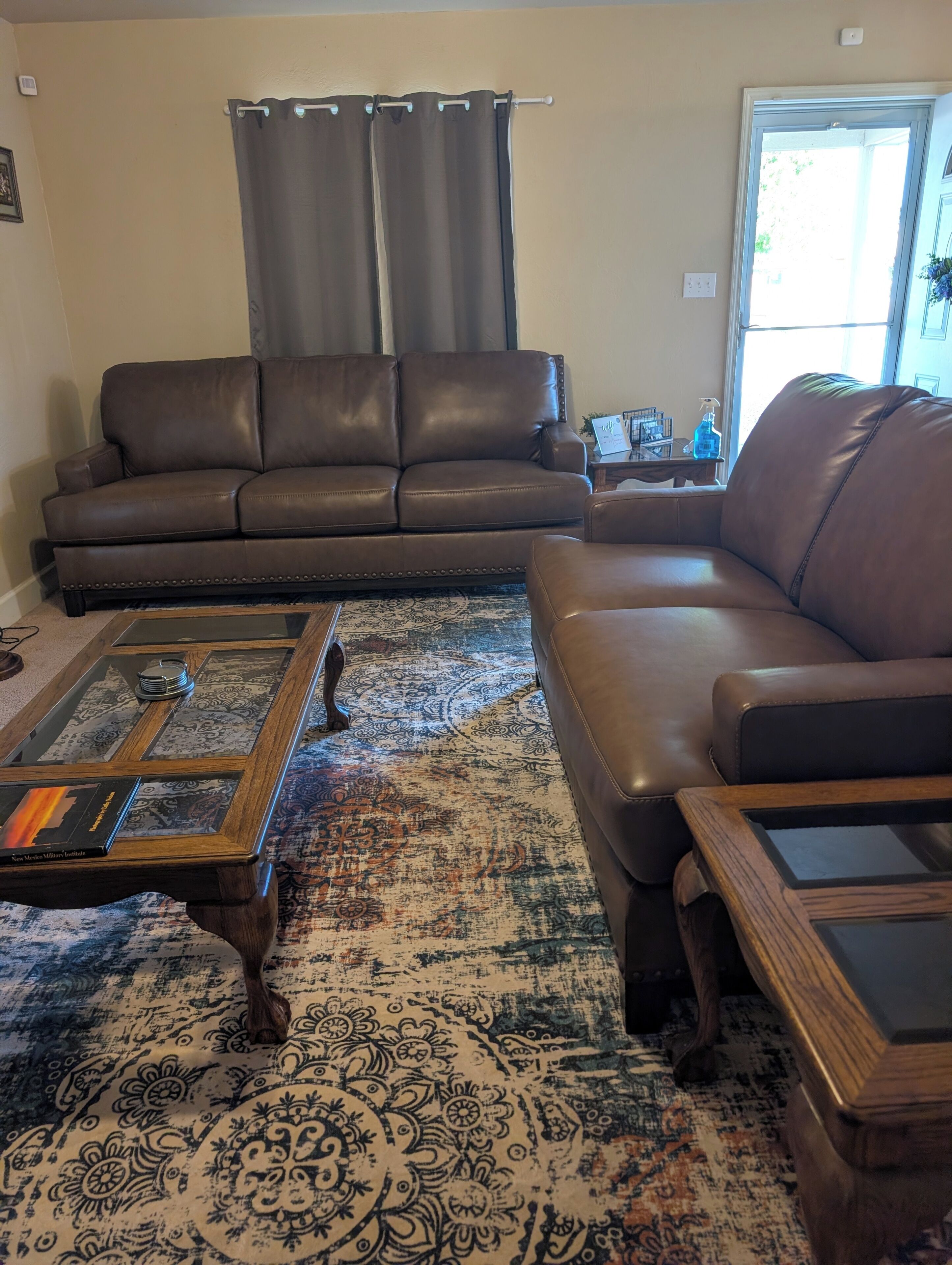 A living room with a brown leather sofa, a glass coffee table, and a patterned rug.