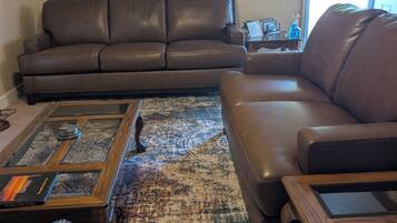 A living room with a brown leather sofa, a glass coffee table, and a patterned rug.