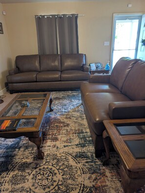 Ein Wohnzimmer mit einem braunen Ledersofa, einem Glastisch und einem gemusterten Teppich.
