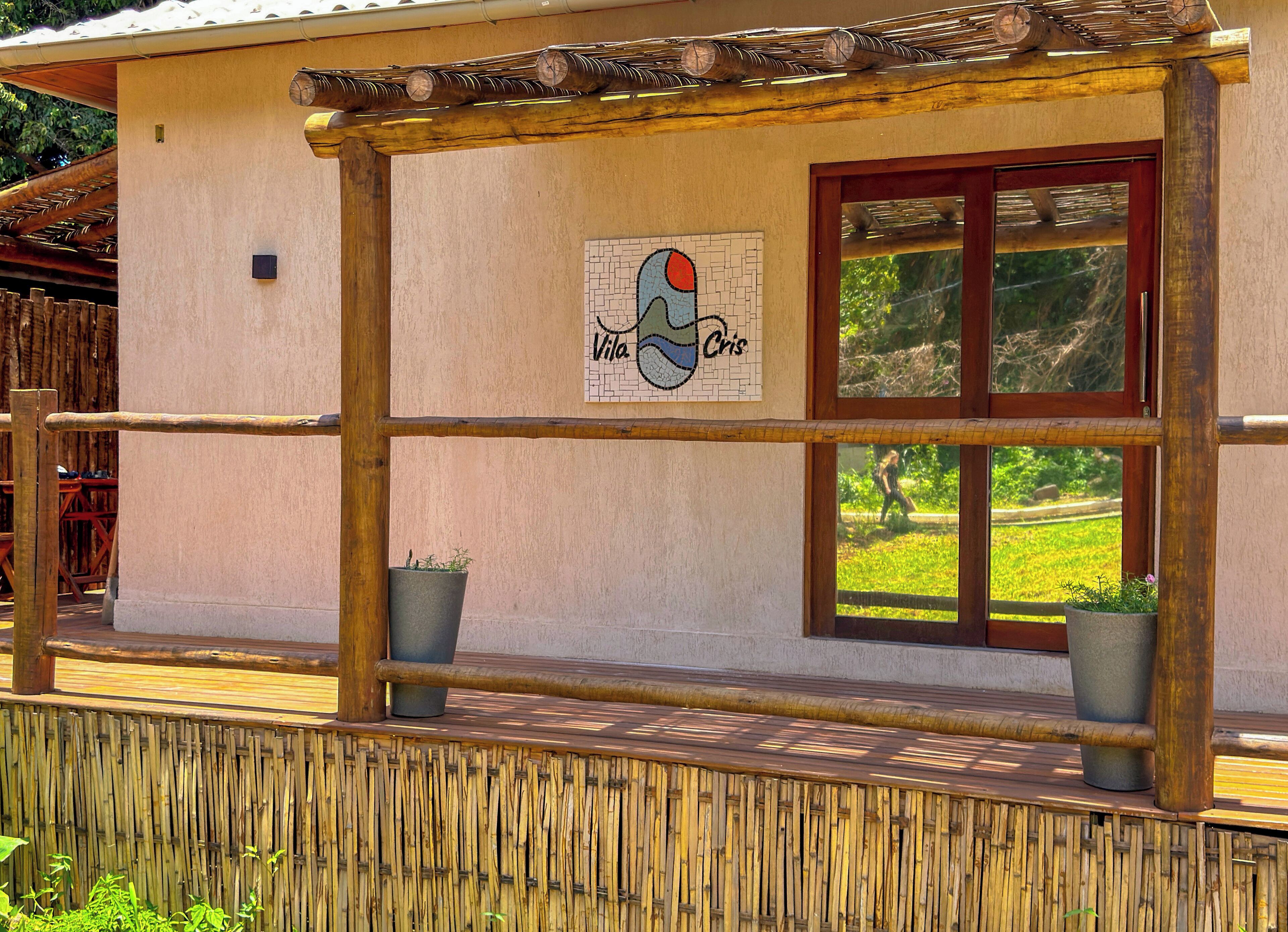Un bâtiment agrémenté d’une pergola en bois, d’une fresque murale portant l’inscription « Vila Cris » et de deux plantes en pot.