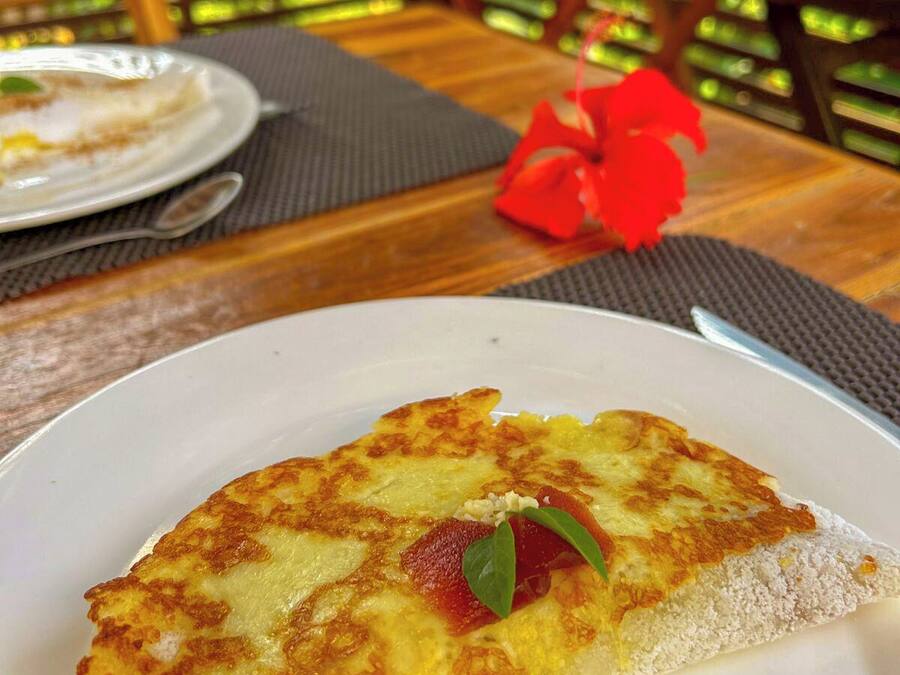 A dining table with a plate of food, a red flower, and a drink in the background.