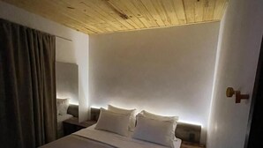 A hotel room with a wooden ceiling, a bed with white linens, a nightstand, a lamp, and a door with a keyhole. - VILLA CRIS (Fernando de Noronha)