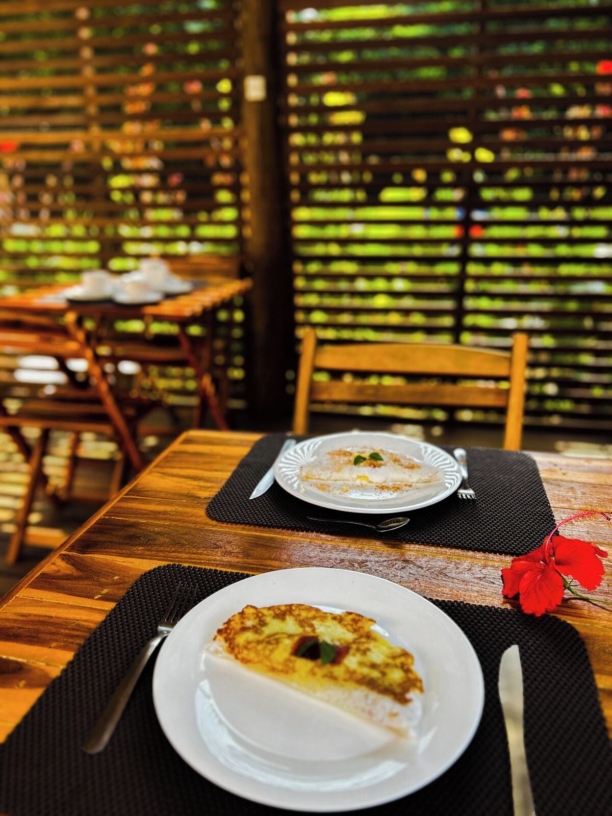 Una mesa de madera con dos platos de comida, un cuchillo y una flor roja sobre un camino de mesa negro.