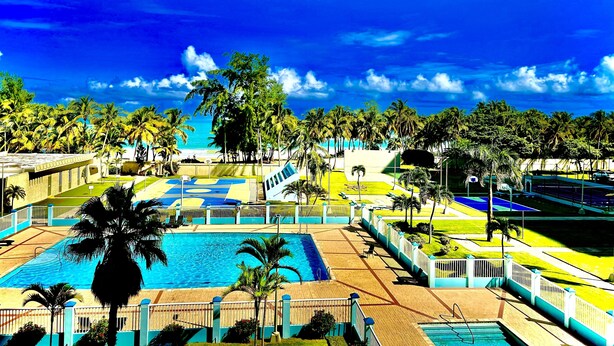 Et resort med swimmingpool, palmer og havudsigt.