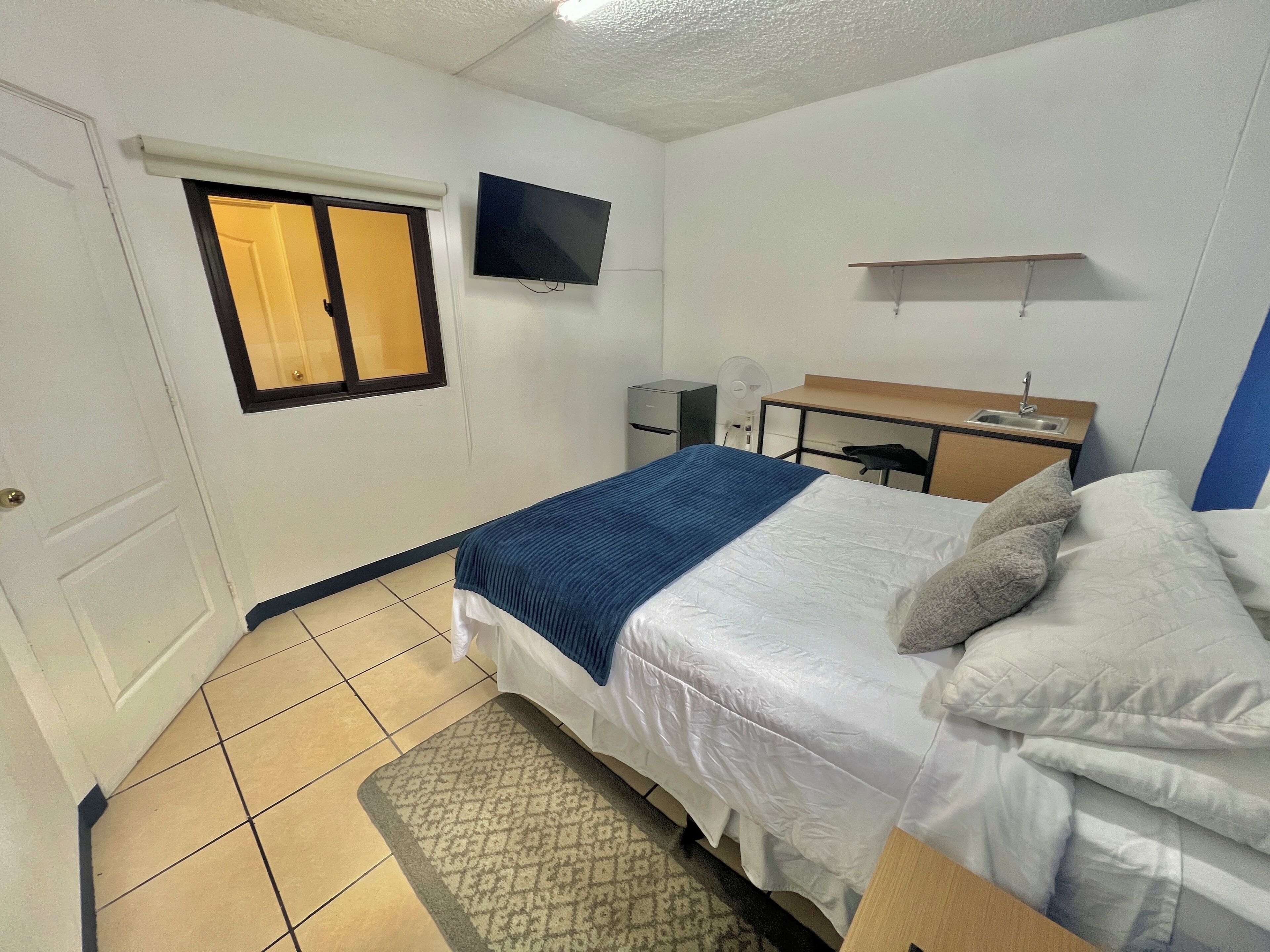 A hotel room with a bed, a desk, a chair, a TV, and a window.