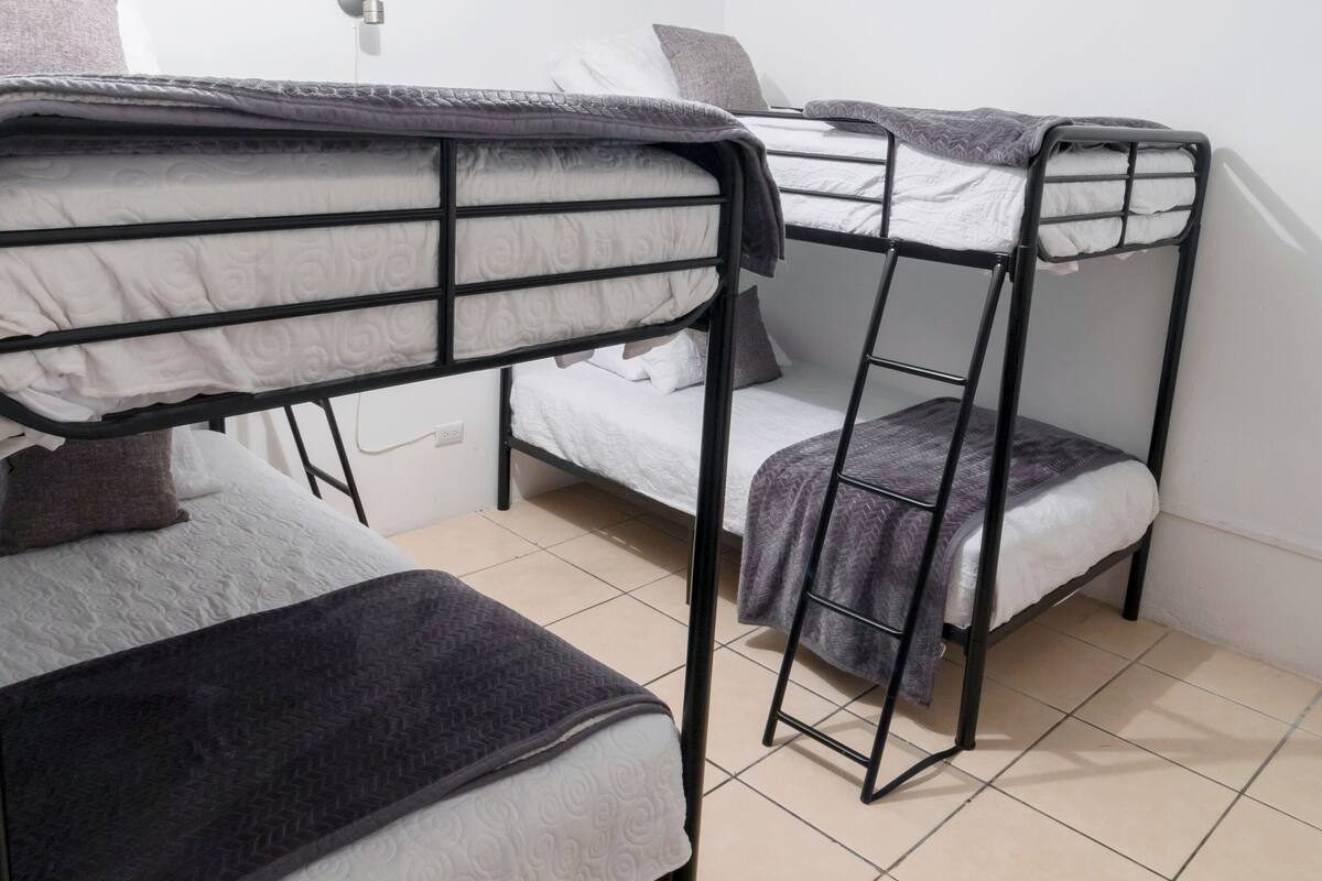 A dormitory room with bunk beds, a bedside table, and a wall-mounted light.