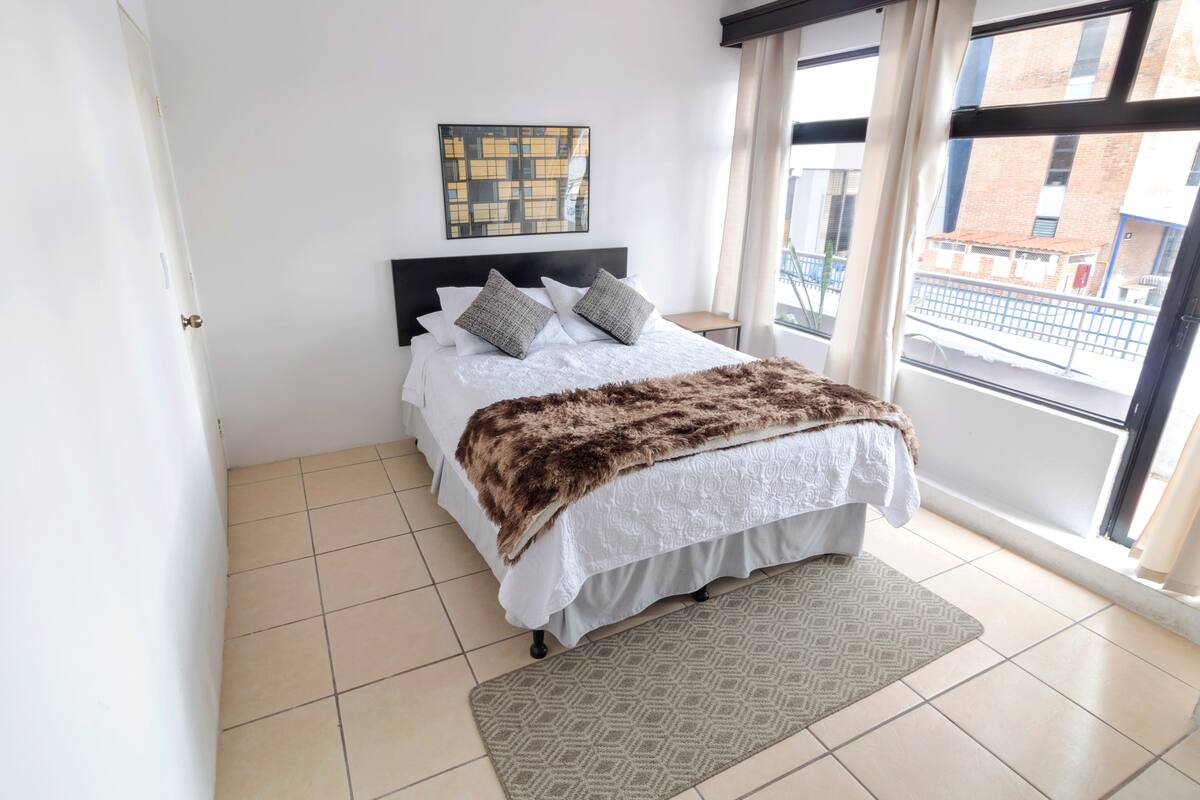 A bedroom with a bed, a window, and a view of buildings outside.