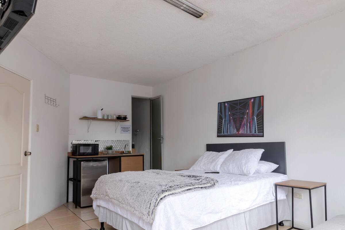 A bedroom with a bed, bedside table, and a small desk with a microwave.