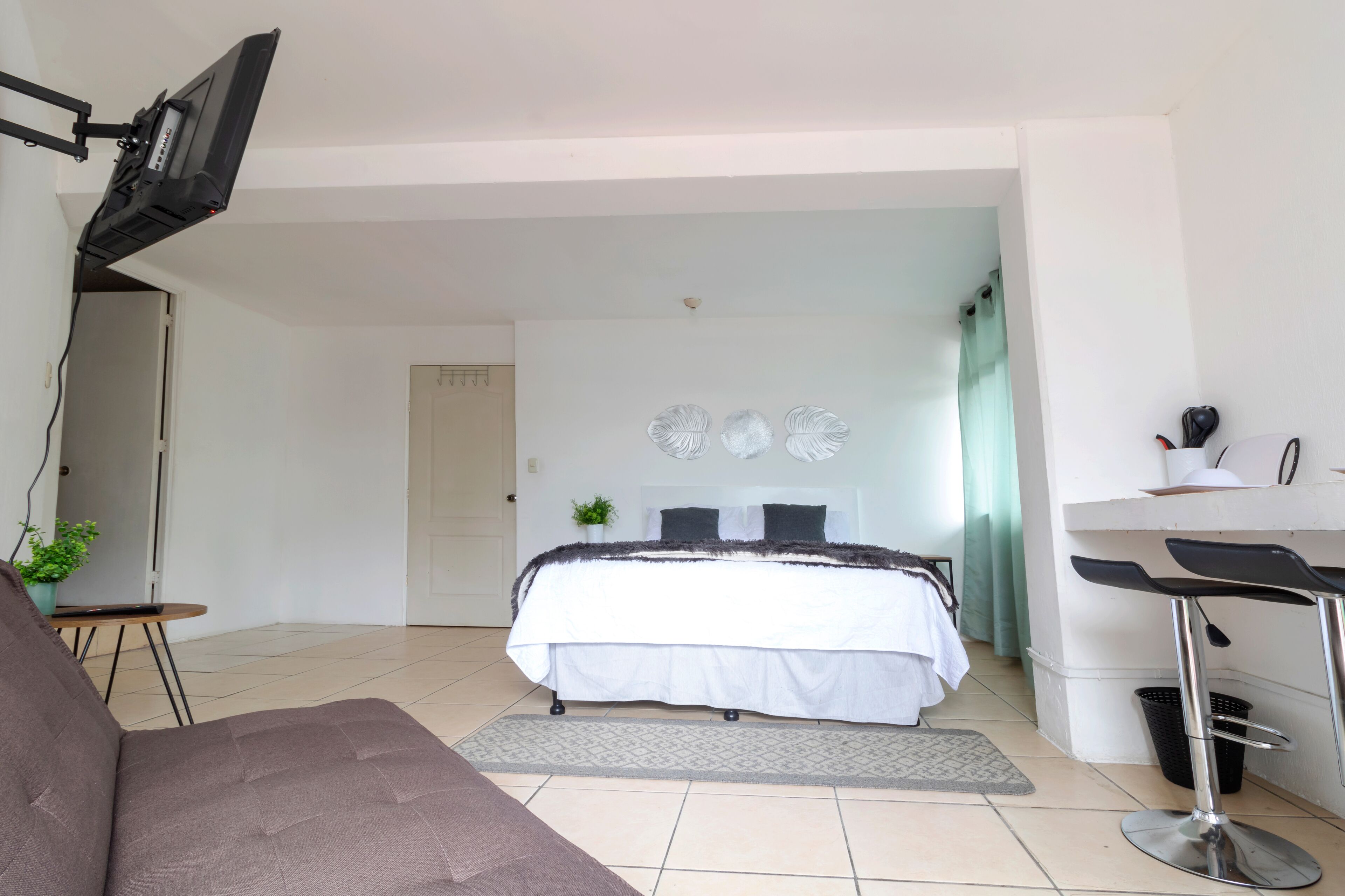 Une chambre à coucher avec un lit, un bureau, une chaise, une télévision et une plante.