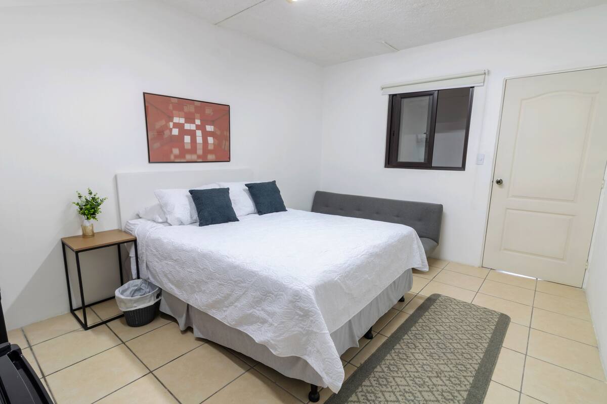 A bedroom with a bed, bedside table, and a small plant.