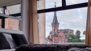 A view of a church with a tall spire and crosses from a window overlooking a bed with black and white bedding. - Hotel Citadin Z4 (Guatemala City)