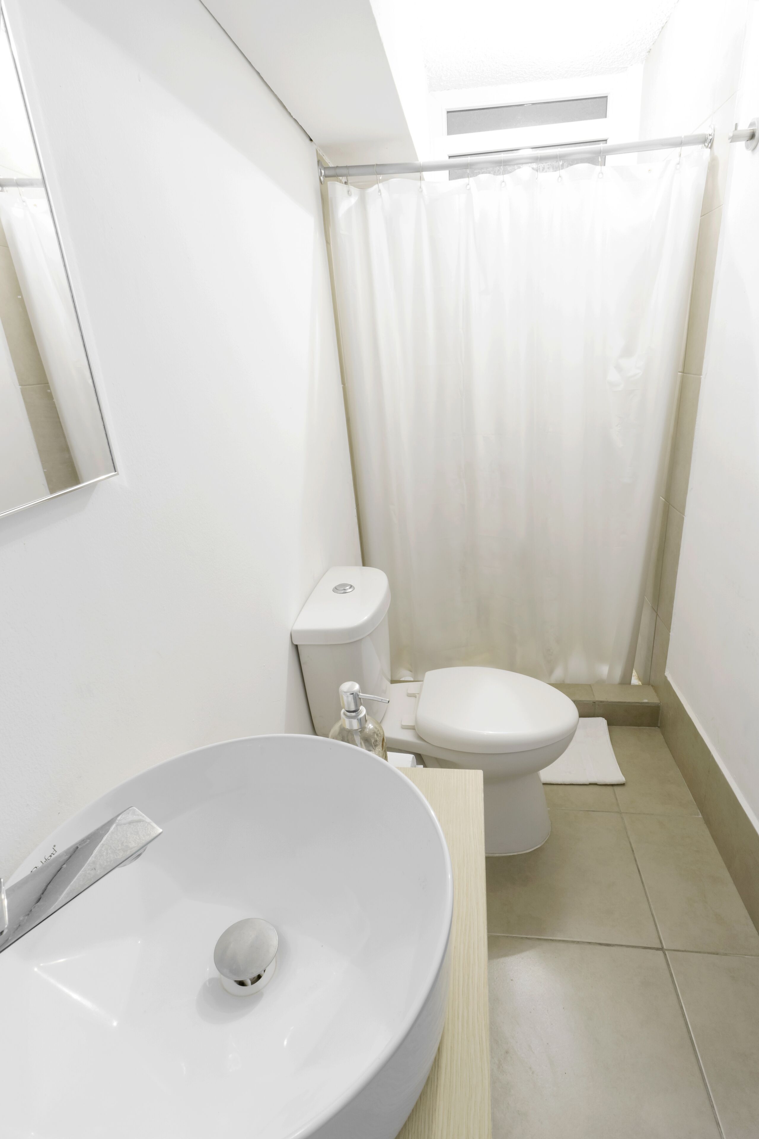 Un baño pequeño y moderno con lavamanos, inodoro y cortina de ducha blancos.
