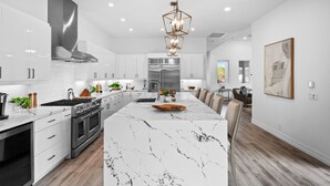A modern kitchen with white cabinetry, a large island, stainless steel appliances, and a pendant light.