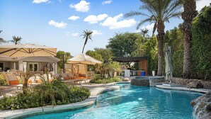 A pool area with lounge chairs, umbrellas, and a waterfall feature.