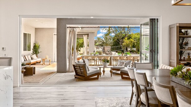 A spacious living area with a large sliding glass door leading to an outdoor patio. The room features a modern sofa, a dining table with chairs, and a coffee table.