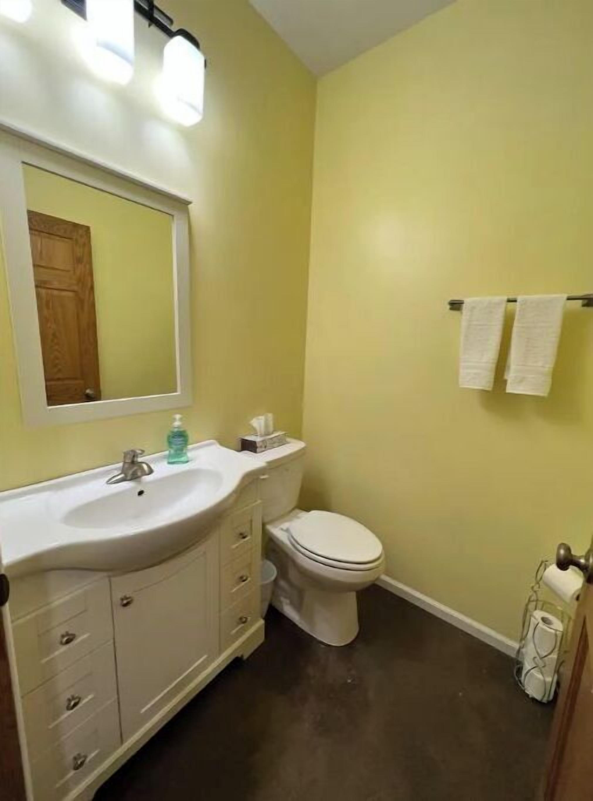A bathroom with a white sink, mirror, and toilet. There are two towels hanging on a rack.
