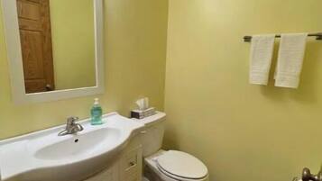 A bathroom with a white sink, mirror, and toilet. There are two towels hanging on a rack.