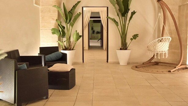 A cozy lounge area with wicker furniture, potted plants, and a hanging chair. - LeVolte luxury apartment and pool (Sternatia)