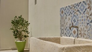 A stone bench, a potted plant, and a tiled wall with a faucet. - LeVolte luxury apartment and pool (Sternatia)