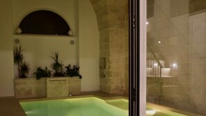 An indoor swimming pool with a stone wall and arched ceiling, surrounded by potted plants. - LeVolte luxury apartment and pool (Sternatia)