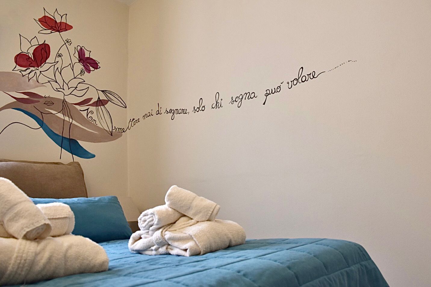 Ein Schlafzimmer mit einem Bett, blauer Bettwäsche und einer Wanddekoration mit einem Zitat und floralem Design.