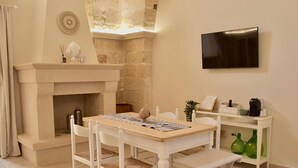 A cozy room with a fireplace, a dining table with chairs, a television, and a small shelf with items. - LeVolte luxury apartment and pool (Sternatia)