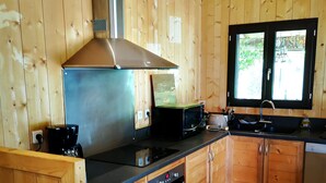 A kitchen with wooden cabinetry, a stove, a microwave, and a sink. - Pleasant wooden house near beaches and forest (Le Porge)