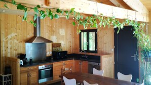 A wooden cabin interior with a kitchen, dining area, and a large window. - Pleasant wooden house near beaches and forest (Le Porge)