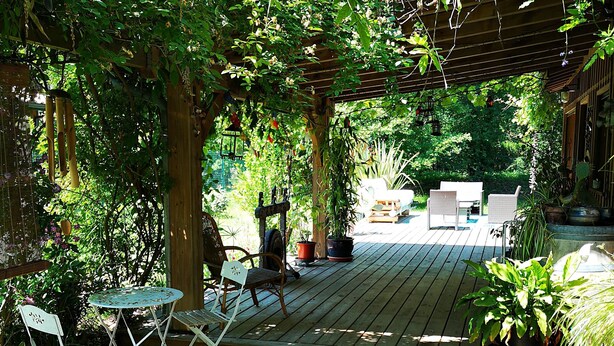 A wooden deck with a pergola, surrounded by lush greenery and potted plants. - Pleasant wooden house near beaches and forest (Le Porge)