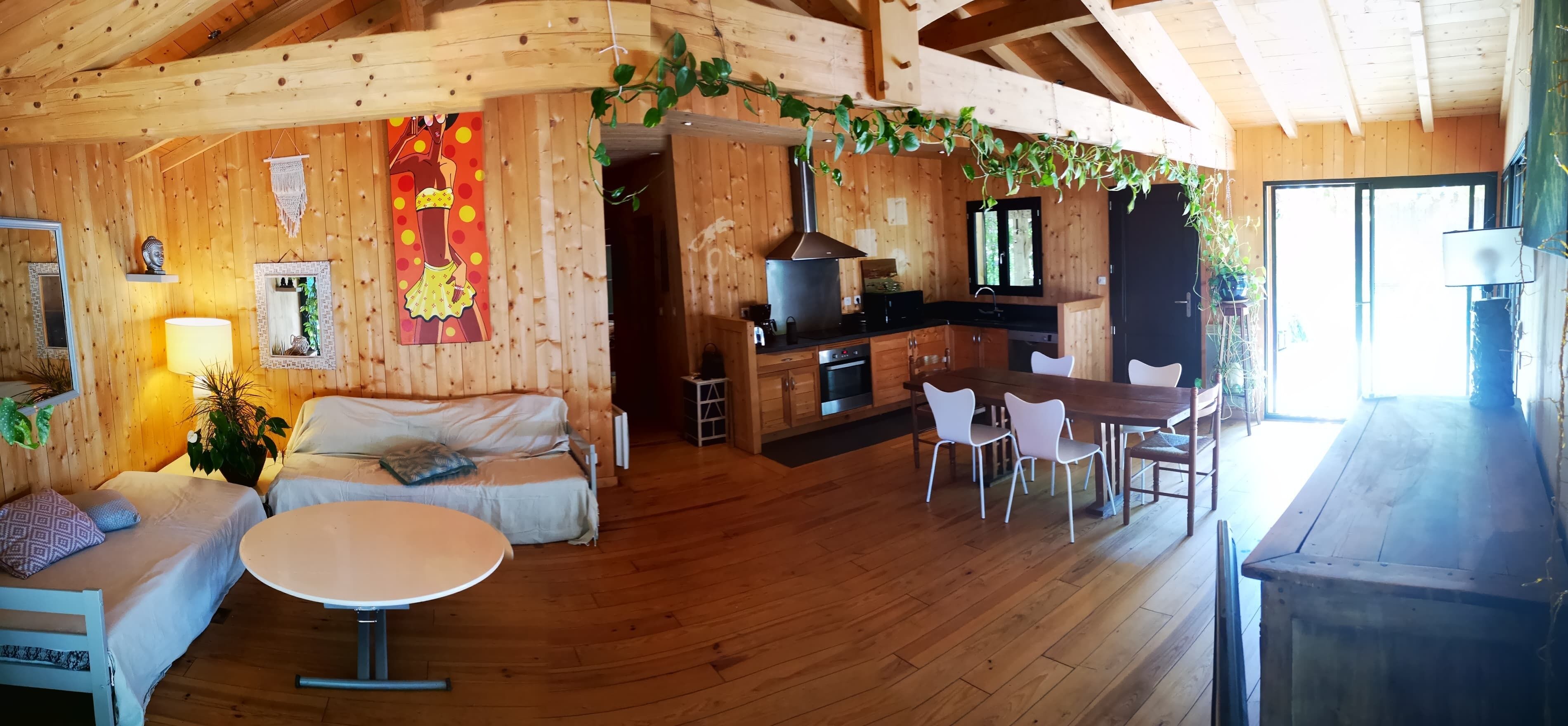 Ein gemütliches Blockhaus-Interieur mit Holzwänden, einer Essecke, einer Küche und einem Wohnzimmer mit Sofa und Tisch.