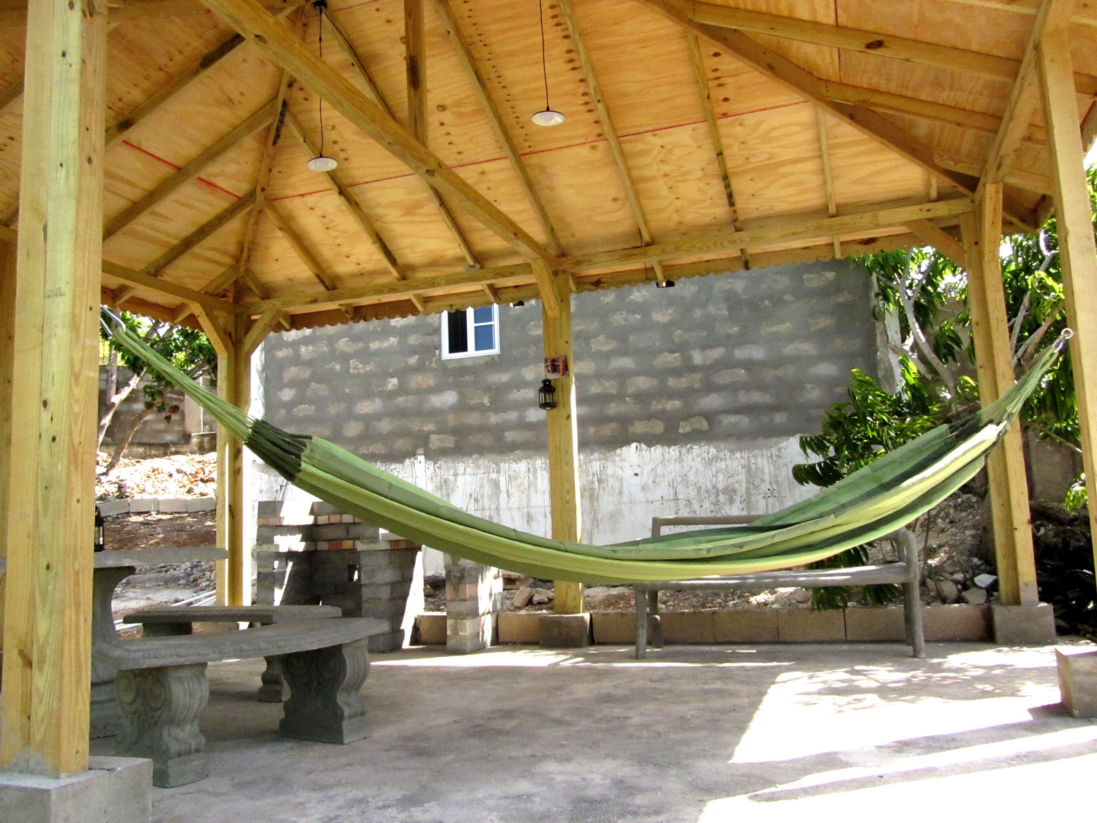 A covered outdoor area with a hammock, a stone bench, and a stone wall in the background.