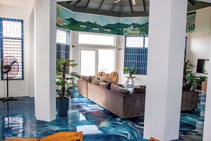Una habitación con piso azul, un sofá, un ventilador y una ventana con barrotes.