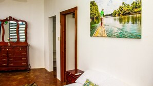 Ein Schlafzimmer mit einem Bett, einer hölzernen Kommode, einem Spiegel und einem Gemälde einer Flusslandschaft.