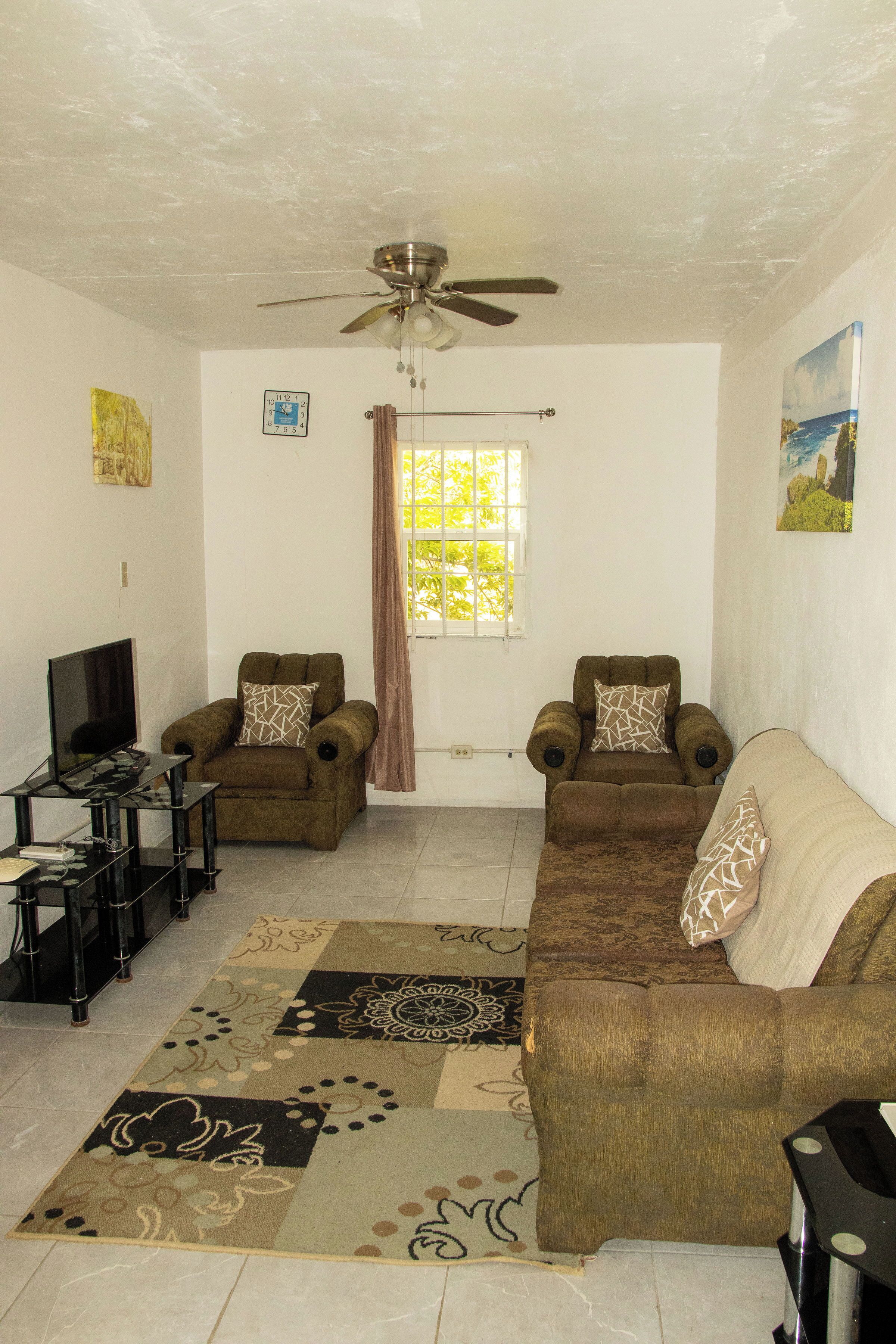 A living room with two sofas, a television, a ceiling fan, and a window with curtains.