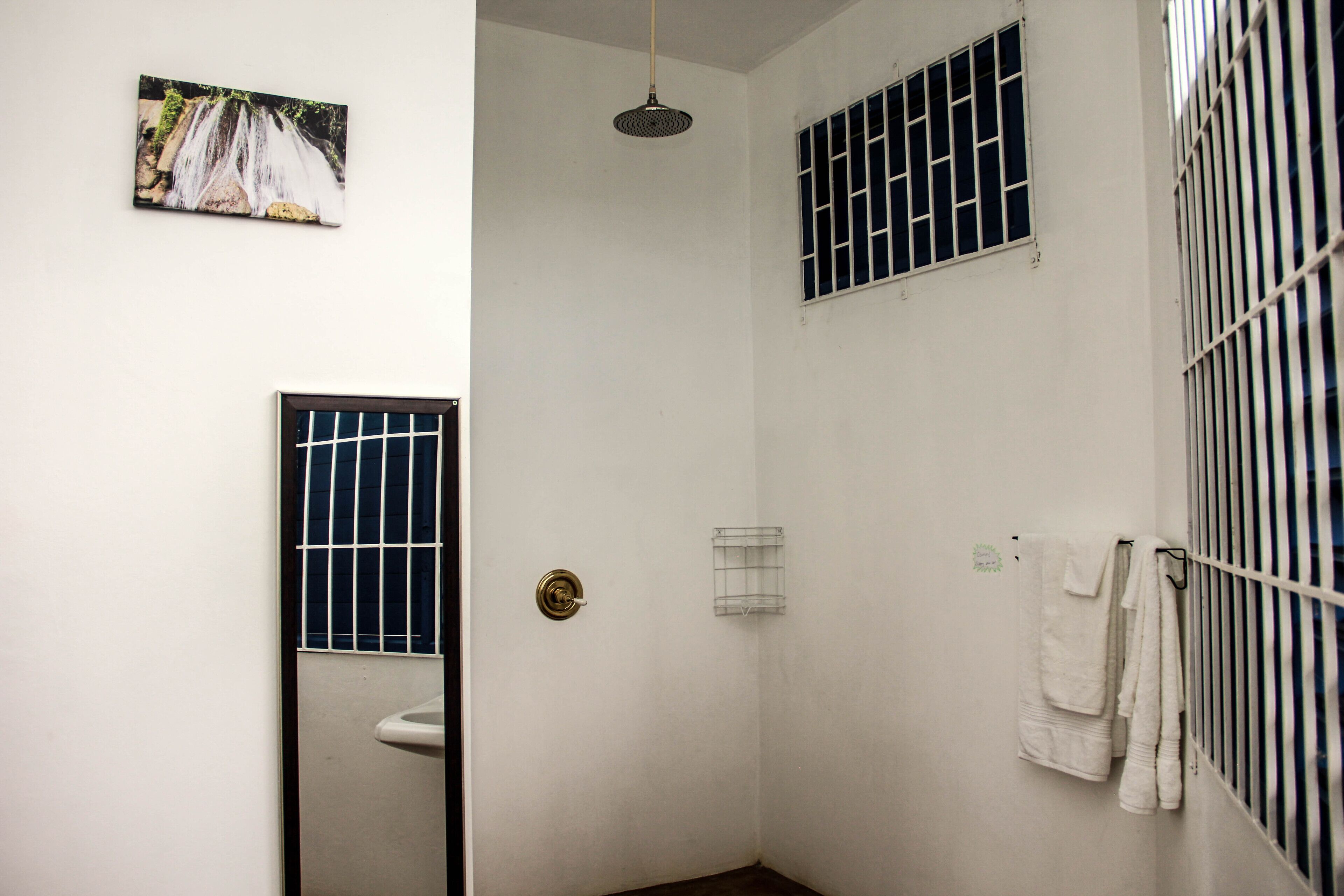 Un espacio de ducha pequeño y cerrado con un inodoro, un perchero y una ventana con barrotes.