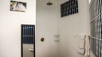 Un espacio de ducha pequeño y cerrado con un inodoro, un perchero y una ventana con barrotes.