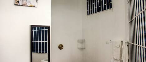 A small, enclosed shower area with a toilet, a towel rack, and a window with bars.