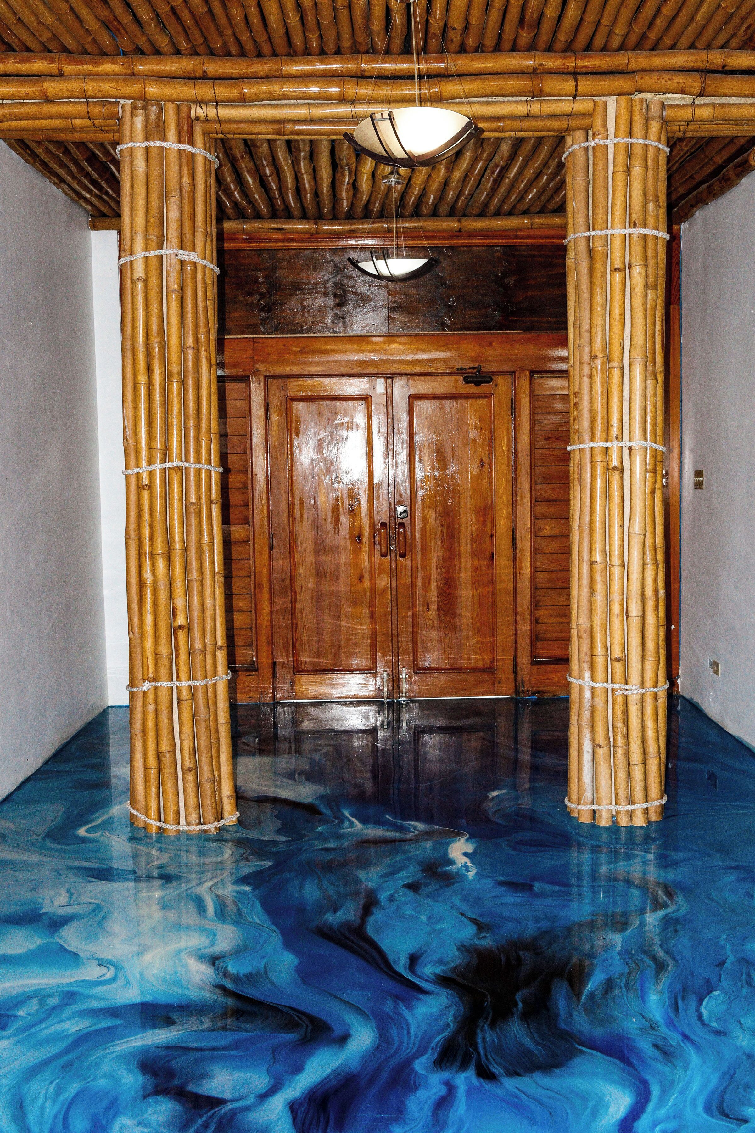 Une pièce dotée d’une porte en bois, de piliers en bambou et d’un sol orné d’un motif bleu évoquant le marbre.