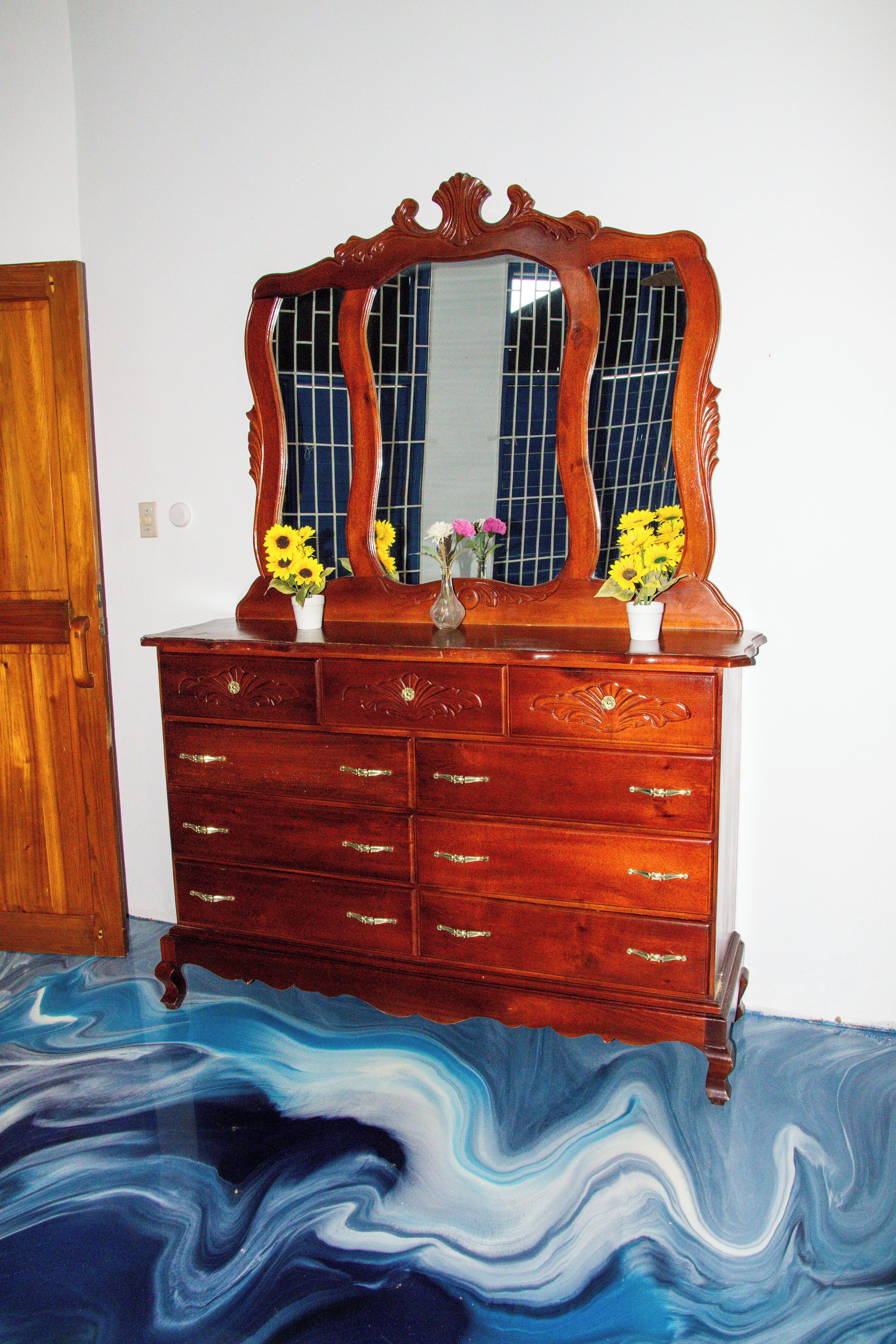 A wooden dresser with a mirror and multiple drawers, positioned against a wall with a blue floor design.