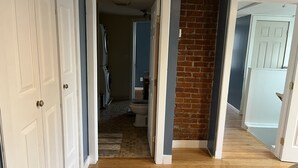 Un pasillo con suelo de madera, pared de ladrillo y puertas blancas que dan a diferentes habitaciones.
