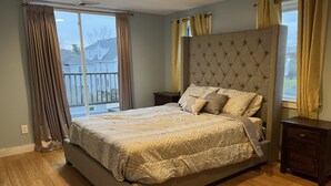 Un dormitorio con una cama grande, una mesita de noche, suelo de madera y vistas al exterior.