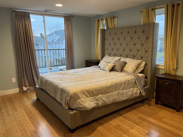 Ein Schlafzimmer mit einem großen Bett, einem Nachttisch, Holzboden und Blick ins Freie.