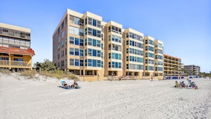 A beachfront hotel with multiple floors, balconies, and a sandy beach area. - Madeira Vista 601-Corner Unit, Panoramic View (Madeira Beach)