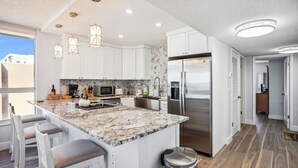 A modern kitchen with white cabinets, a marble island, stainless steel appliances, and pendant lighting. - Madeira Vista 601-Corner Unit, Panoramic View (Madeira Beach)