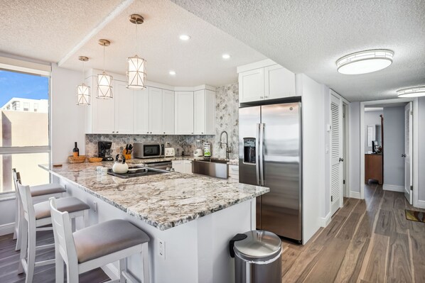 A modern kitchen with white cabinets, a marble island, stainless steel appliances, and pendant lighting.