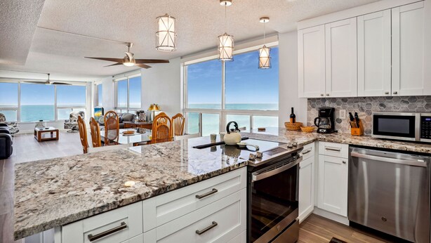 A modern kitchen with granite countertops, stainless steel appliances, and a view of the ocean. - Madeira Vista 601-Corner Unit, Panoramic View (Madeira Beach)
