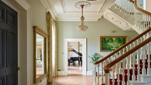 Eine prachtvolle Eingangshalle mit einem Klavier, einer Treppe mit roten Sitzflächen und einer Chandelüster.