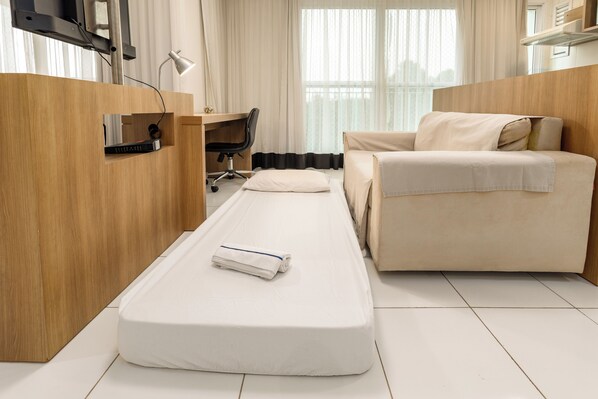 Une chambre d’hôtel de taille réduite, comprenant un lit simple, un bureau, une chaise et un canapé.