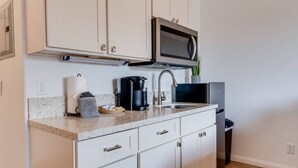 A modern kitchen with white cabinets, a stainless steel microwave, a coffee maker, and a sink. - Unit 16 Waena Inn - Maui Private Suite (Wailuku)
