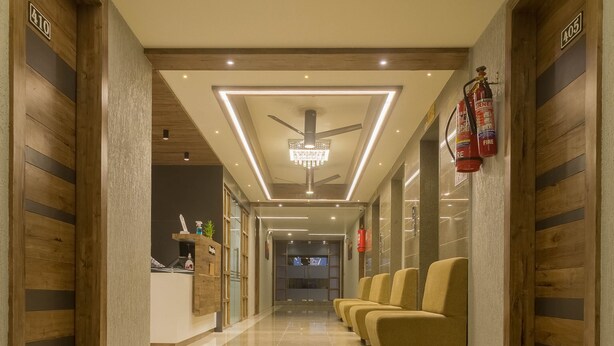A hotel lobby with a polished marble floor, a reception desk, a chandelier, and a row of yellow chairs. - Hotel Green City (Gandhinagar)